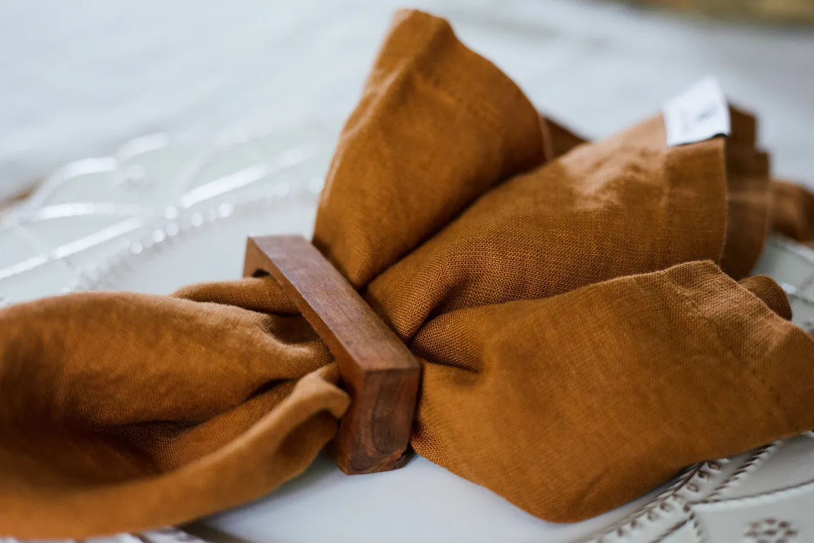 A burnt orange linen napkin in a wooden napkin ring on top of a white porcelain plate
