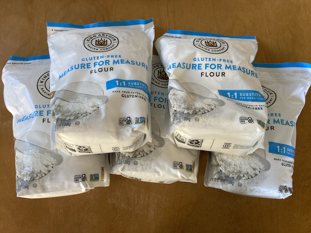 Five bags of King Arthur gluten-free measure for measure flour on a brown tabletop.