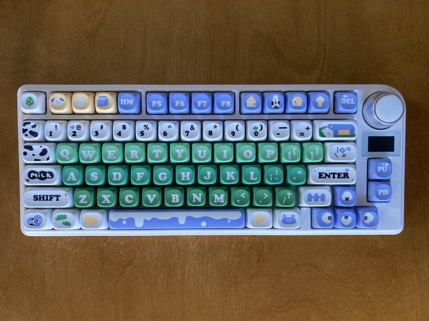 A keyboard with dairy farm-themed keycaps in green, white, blue, and yellow.